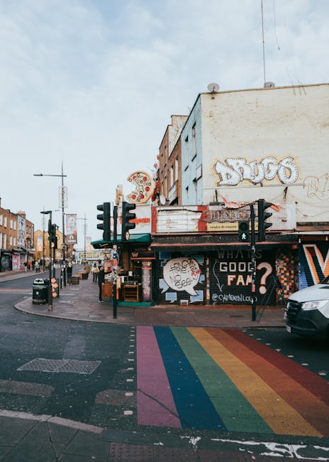 The image depicts a busy urban street scene in Camden Town, with a large, multi-story brick building on the left featuring several arched windows, including a prominent upper-floor window with a semi-